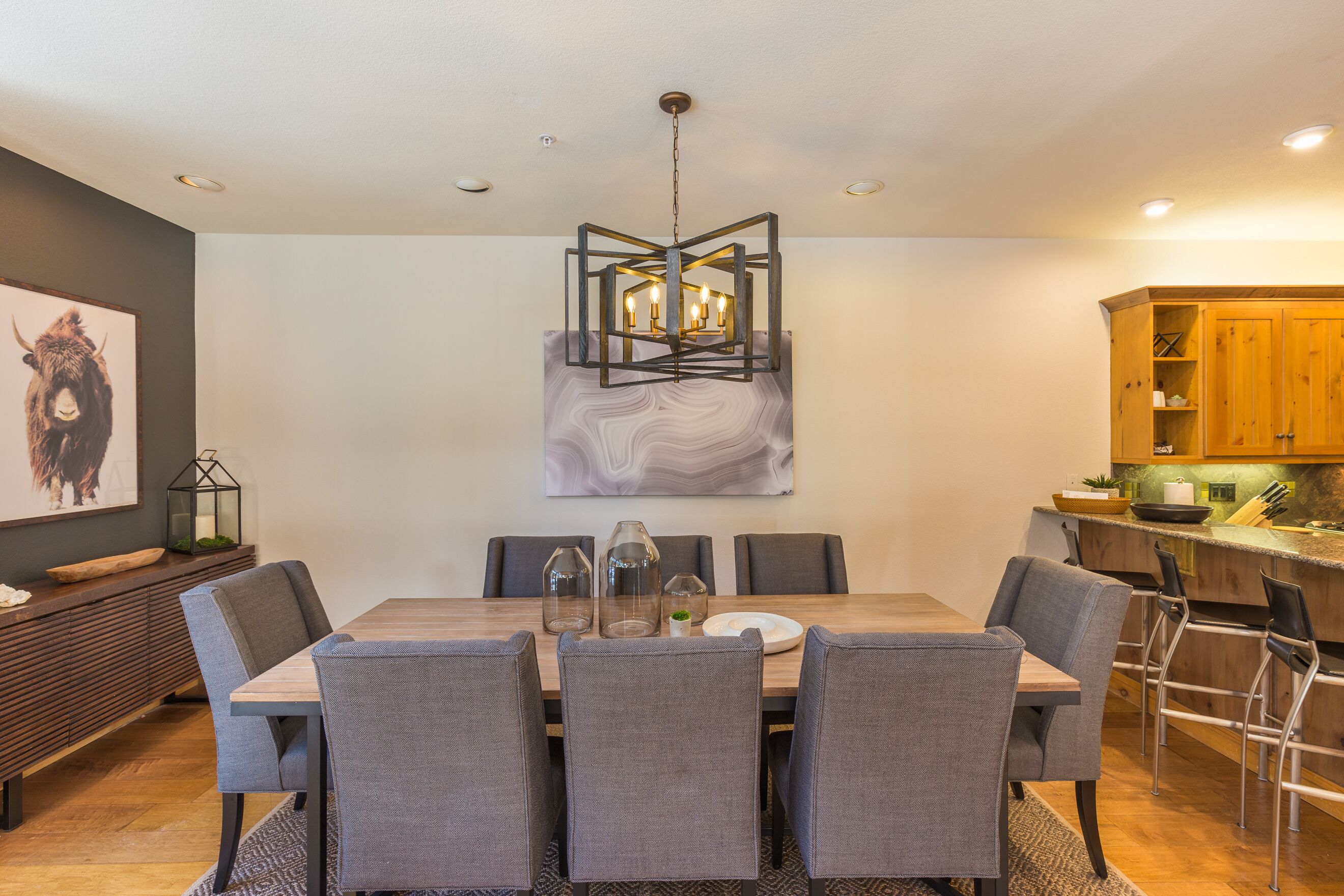 A modern dining area with a wooden table, grey upholstered chairs, and a geometric pendant light.