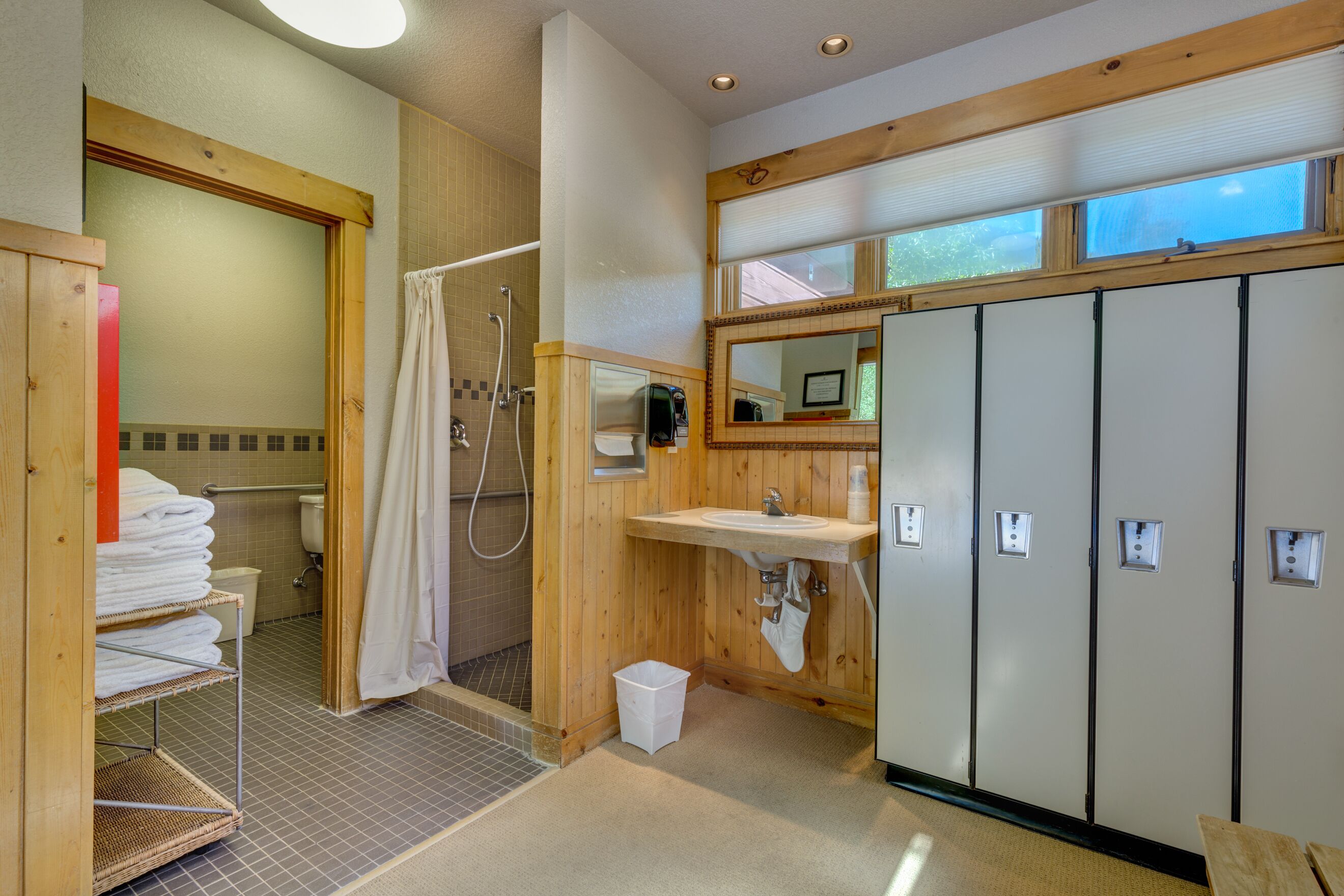 Une salle de bain équipée d’une douche, de toilettes, d’un lavabo et de casiers en bois.