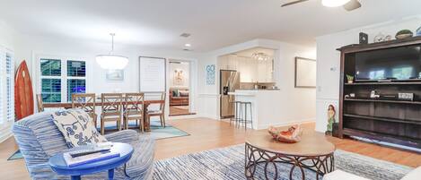A modern living room with a sofa, coffee table, and a bookshelf. There is a dining area with a table and chairs.