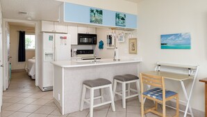 Uma cozinha compacta com armários brancos, uma ilha central com banquetas, micro-ondas e pia.