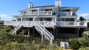 A multi-story beachfront house with a balcony, stairs, and a covered deck area.