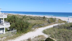 A beachfront property with a sandy path leading to the beach, a fenced area, and a building with a balcony.