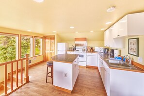 A kitchen with white cabinets, a central island, and a view of greenery through large windows.