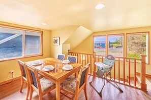 A dining area with a wooden table set for four, a high chair, and a view of a playground through large windows.