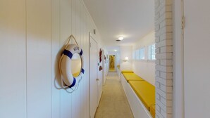 Un pasillo con un flotador en la pared, un banco amarillo y una pared de ladrillo blanco.