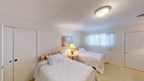 Ein Zimmer mit zwei Betten, einem Bild an der Wand, einem Fenster mit Vorhängen und einer Deckenleuchte.