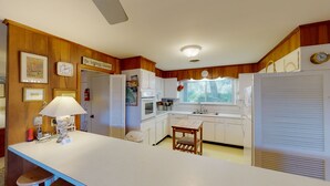 Una cocina con paneles de madera, una encimera blanca, un fregadero, una estufa y una ventana con persianas.