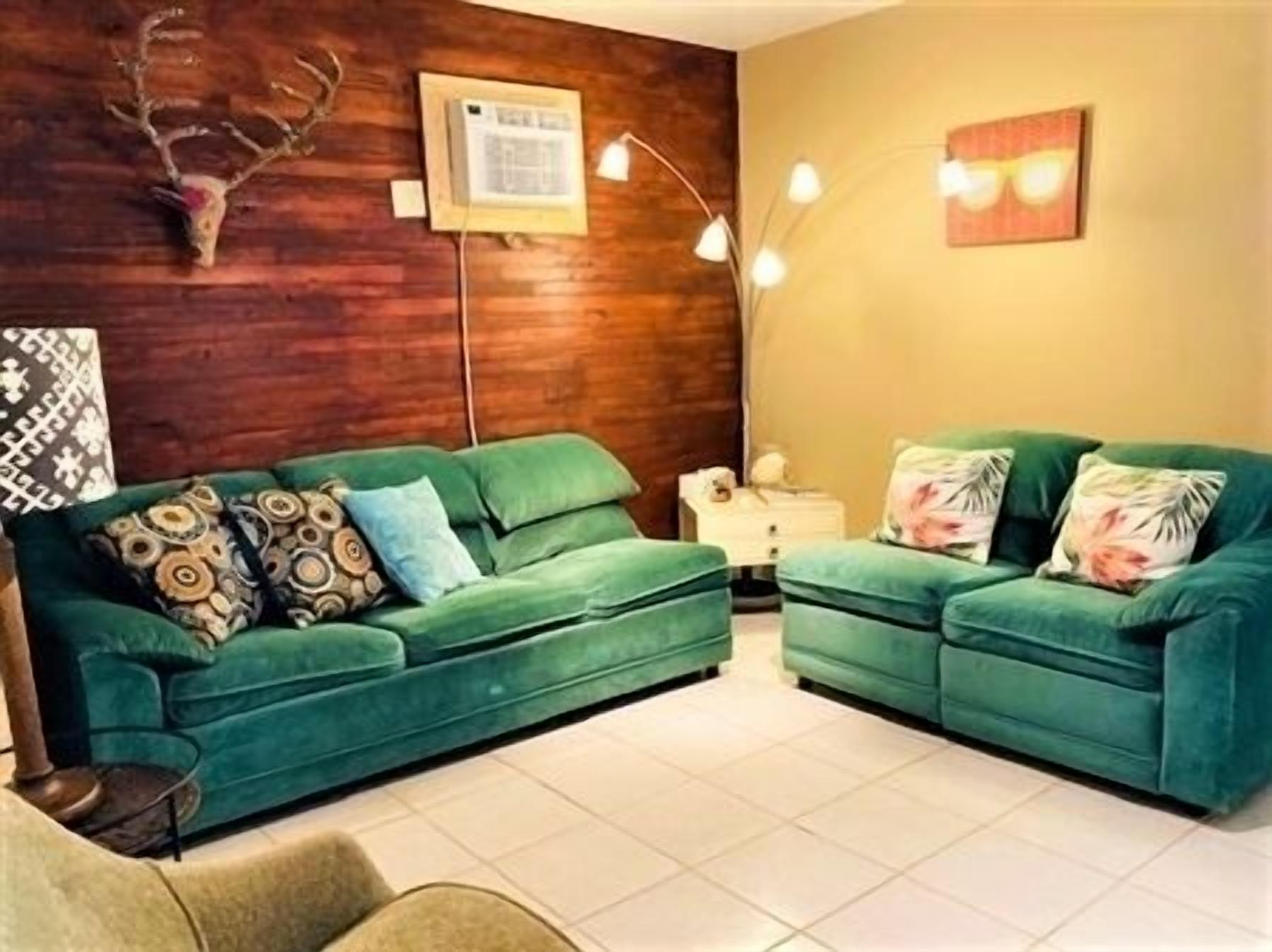 Ein Wohnzimmer mit zwei grünen Sofas, einer Holzwand, einem aufgehängten Hirschgeweih, einer Wandlampe und einem gerahmten Bild.