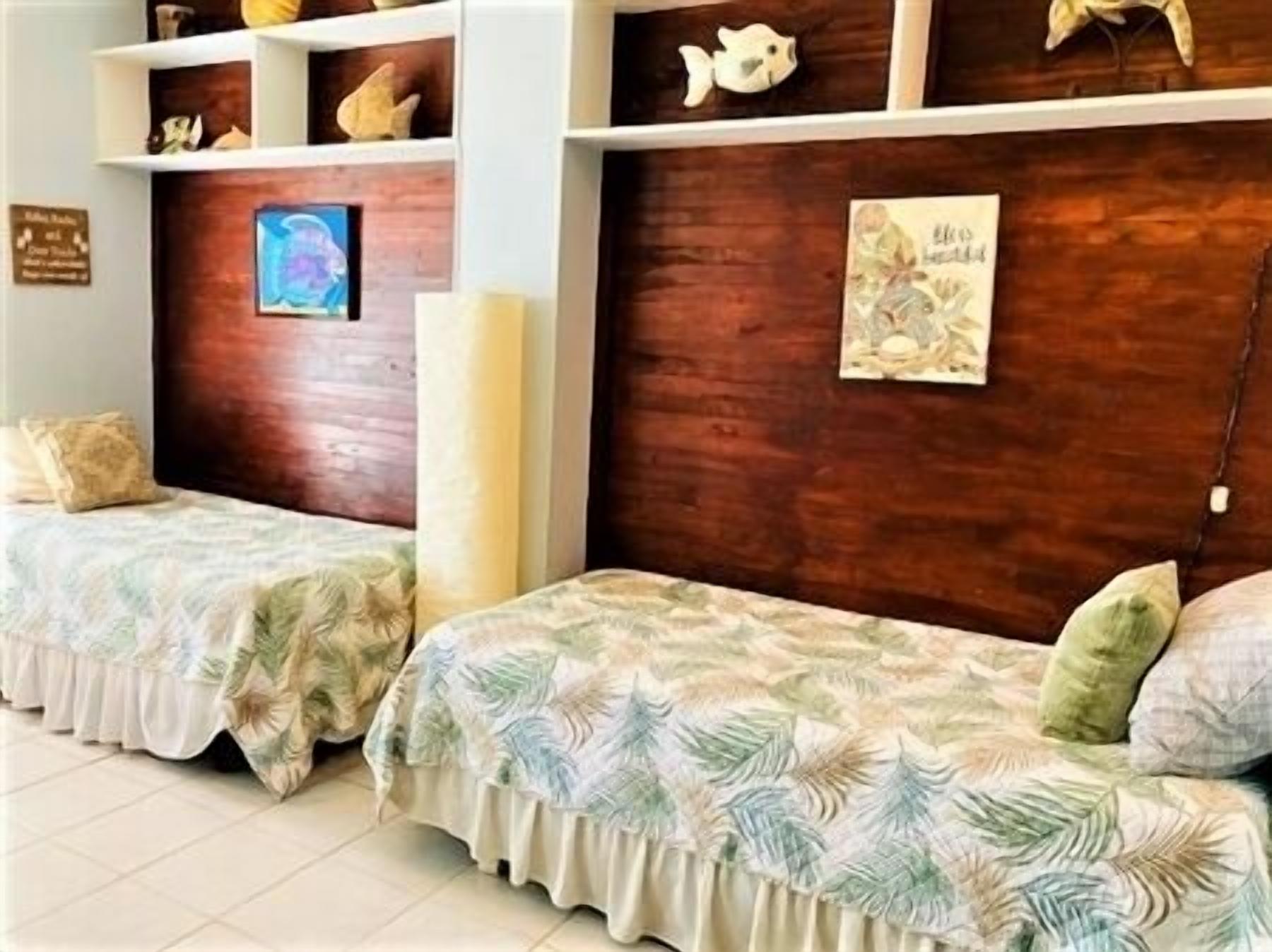 Une chambre d’hôtel avec deux lits, des étagères en bois ornées d’objets décoratifs, un tableau encadré au mur et une pancarte sur la porte.