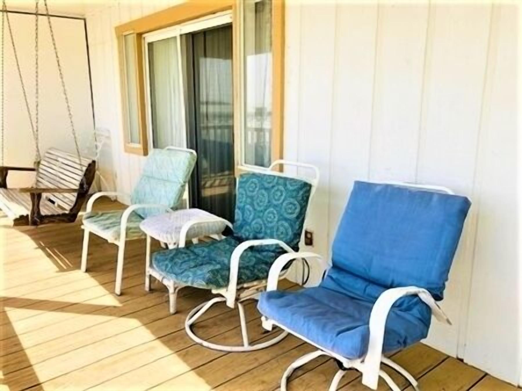 Een houten terras met drie schommelstoelen, één blauw en twee groen, en een hangstoel op de achtergrond.