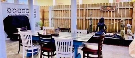 An outdoor dining area with a table and chairs, a grill, and a wooden fence in the background.
