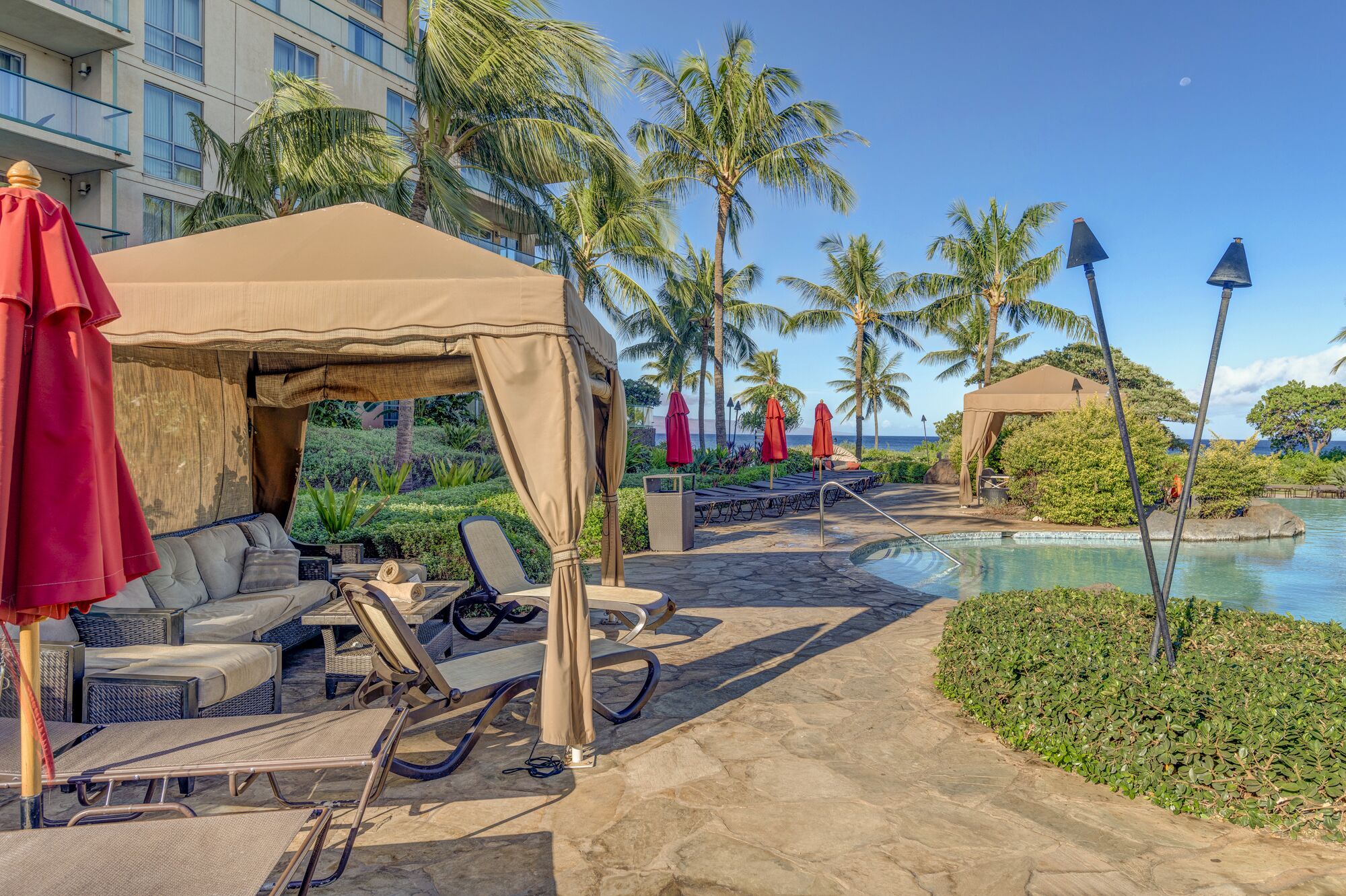 Un área junto a la piscina con sillones de descanso, una pérgola y vista al océano.