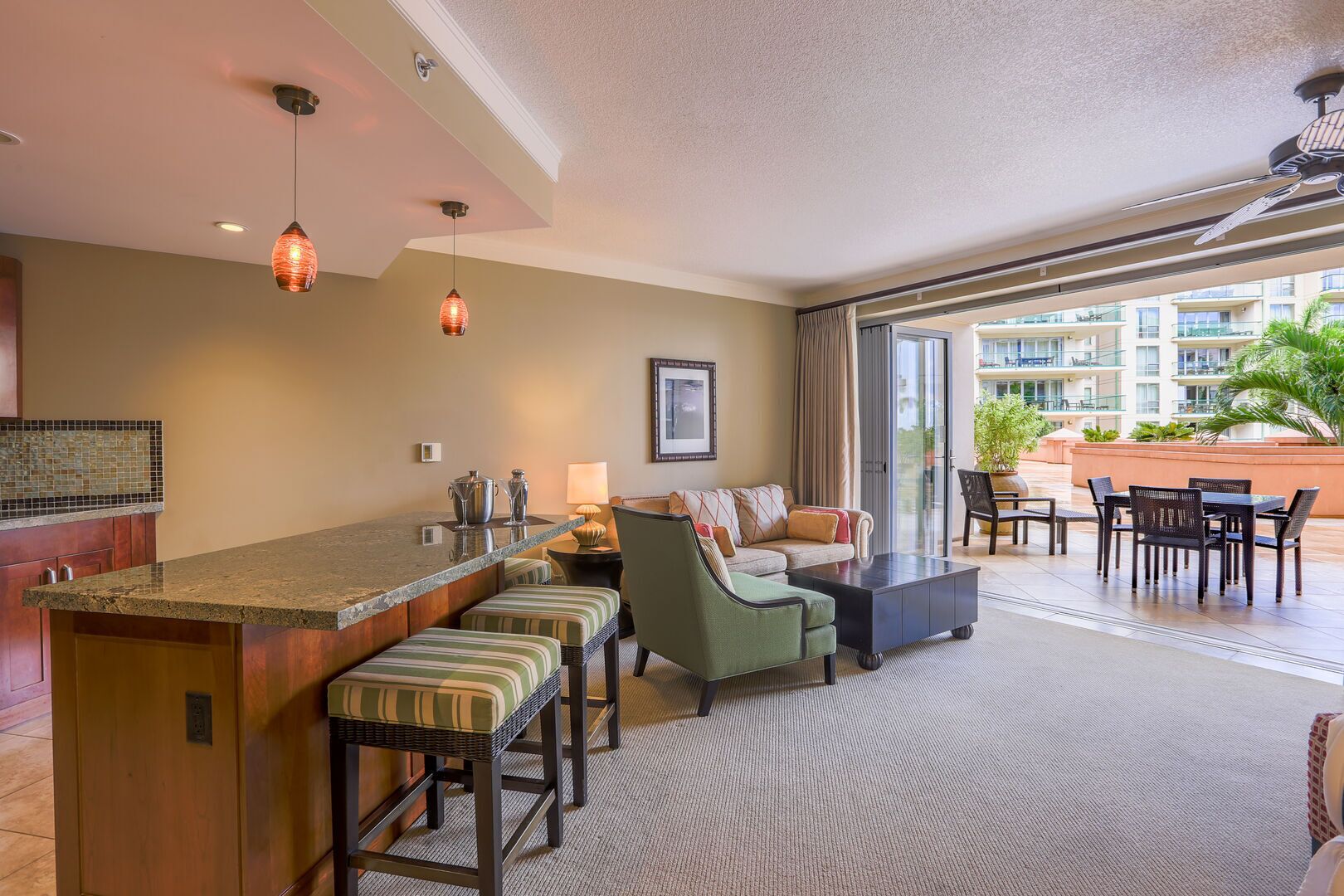 Habitación de hotel con cocina, zona de estar con sofá y sillas, y balcón con mesa y sillas.