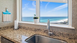 A kitchen with a granite countertop, a stainless steel sink, and a window with a view of the ocean. - Beachfront ~ Penthouse ~ 2 Balconies (Miramar Beach)