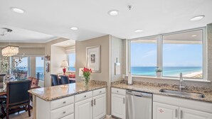A modern kitchen with white cabinets, granite countertops, and a large window offering a view of the beach. - Beachfront ~ Penthouse ~ 2 Balconies (Miramar Beach)