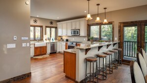Una cocina amplia con suelo de madera, una isla central con taburetes y ventanas grandes que ofrecen vistas al exterior.