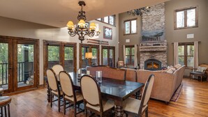 Un comedor amplio con una gran mesa y sillas de madera, una chimenea de piedra y ventanas grandes que ofrecen vistas al exterior.