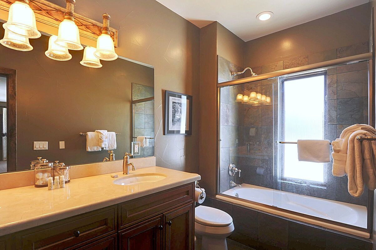 A modern bathroom with a large mirror, two sinks, a toilet, and a bathtub.