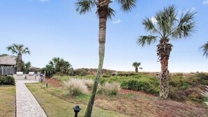 A pathway leading to a building with a thatched roof, surrounded by palm trees and grassy areas. - Ocean One 120 - Beachside Condo (Hilton Head Island)