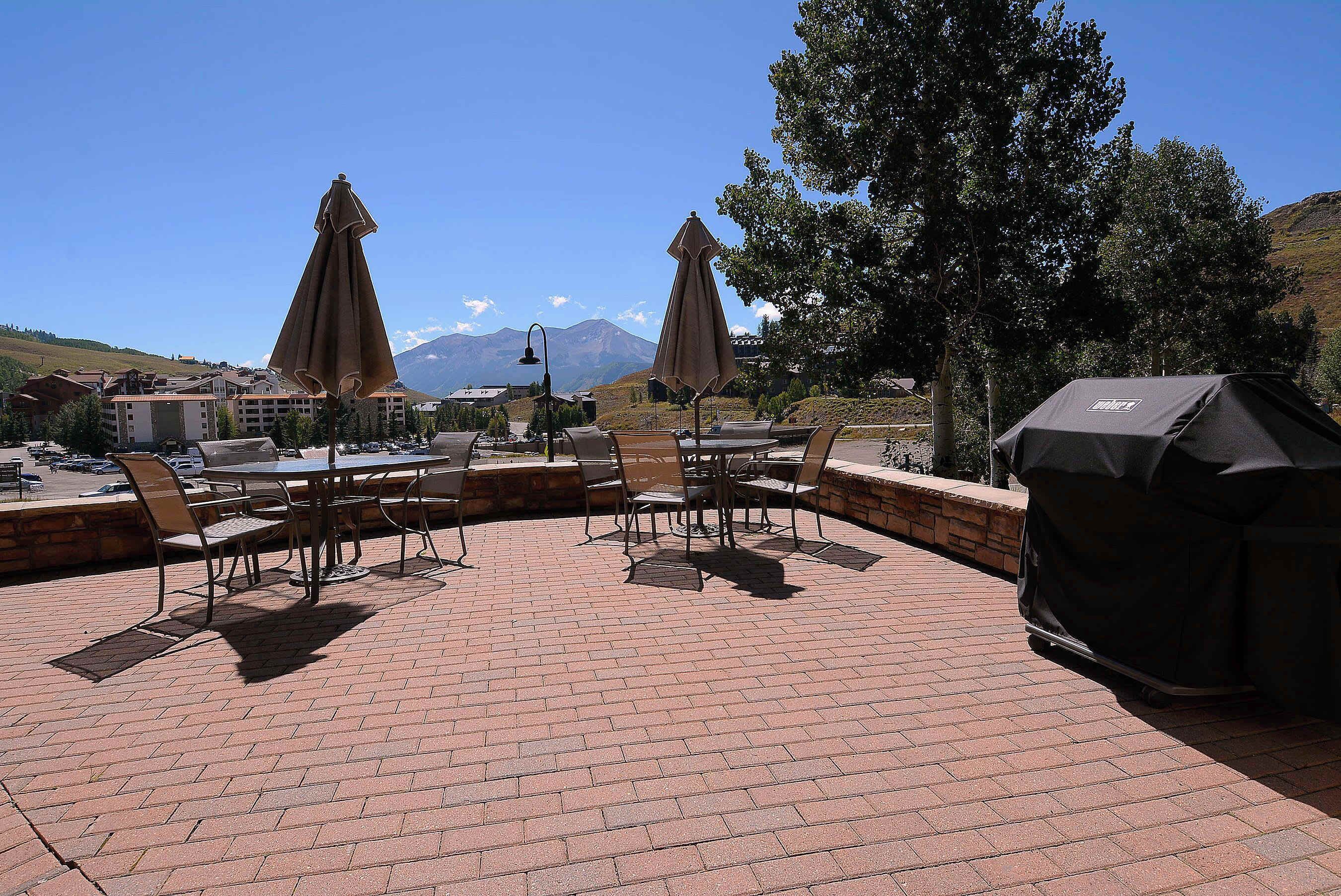 Un patio al aire libre con piso de ladrillo, mesas y sillas de metal, y sombrillas.