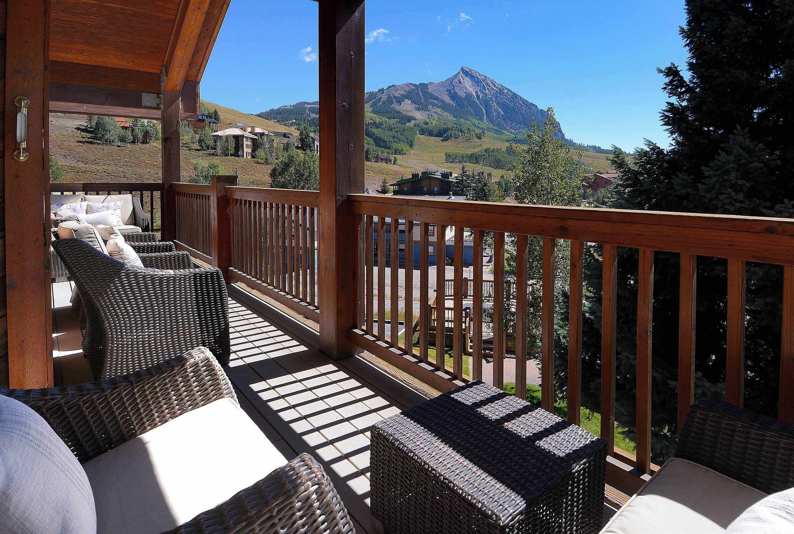 A wooden deck with wicker furniture and a view of mountains.