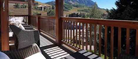 A wooden deck with wicker furniture and a view of mountains.