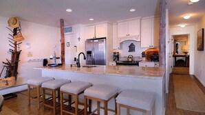 Una cocina con una isla central, taburetes de bar, un refrigerador y una cafetera.