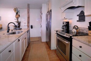 Eine Küche mit weißen Schränken, einem Edelstahl-Kühlschrank, einer Kaffeemaschine und einem Wasserkocher auf der Arbeitsfläche.