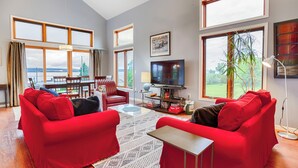 Ein modernes Wohnzimmer mit roten Sofas, einem Fernseher und einem Essbereich mit Blick ins Freie.