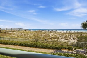 A beach view with a wooden walkway, beach chairs, and a fence.