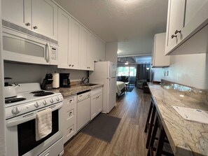 A modern kitchen with white cabinets, a stove, microwave, and a refrigerator. There is a dining area with a table and chairs.