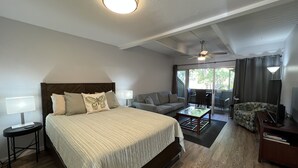 A hotel room with a large bed, a sofa, a coffee table, and a ceiling fan. - Kihei Bay Surf #123 A/C, Wifi, Near Beach, Great Rates, Shared Hot Tub (Kihei)