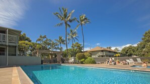 A swimming pool with clear blue water, surrounded by palm trees and lounge chairs. - Kihei Bay Surf #123 A/C, Wifi, Near Beach, Great Rates, Shared Hot Tub (Kihei)