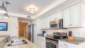 A modern kitchen with granite countertops, stainless steel appliances, and white cabinetry. - Captains Watch 11 | Rooftop Pool, 1 Block to Beach (Tybee Island)