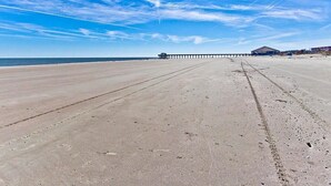 A beach with a pier extending into the water, a covered area, and a clear sky. - Captains Watch 11 | Rooftop Pool, 1 Block to Beach (Tybee Island)