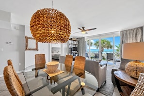Relax in a spacious room with a sofa, armchairs, and a glass dining table, offering a view of the beach and ocean from the balcony.