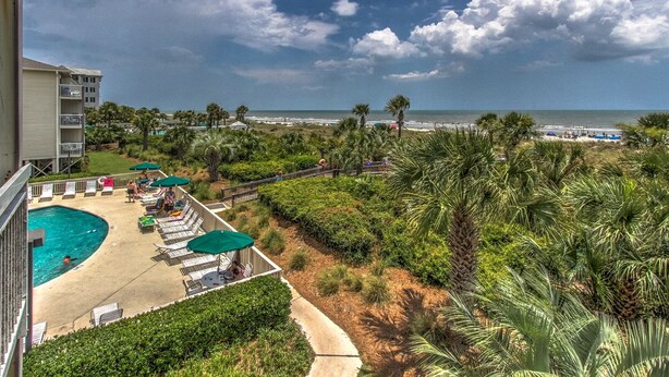 Ein Resort mit Swimmingpool, Liegestühlen und Blick auf Strand und Meer.