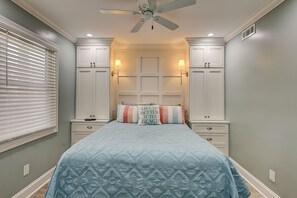 Une chambre à coucher comprenant un lit, des tables de chevet, un ventilateur de plafond et des lampes fixées au mur.