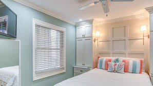 Ein Schlafzimmer mit Bett, einem Fenster mit Jalousien, einem Kleiderschrank und einem Deckenventilator.