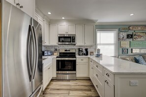 A modern kitchen with stainless steel appliances, white cabinetry, and a herringbone wood floor.
