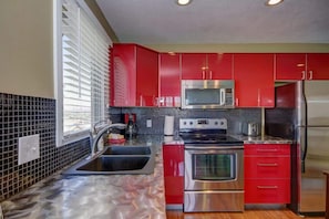 A kitchen with red cabinets, a stainless steel refrigerator, and a microwave.