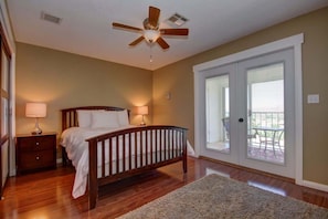 A bedroom with a wooden bed, two bedside lamps, a ceiling fan, and a view of a balcony through a sliding glass door.