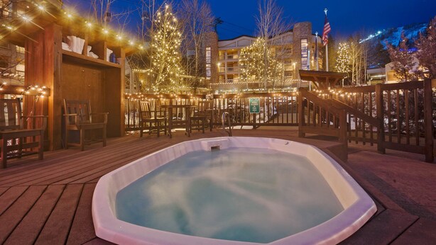 Un bain à remous sur une terrasse en bois, illuminé de guirlandes lumineuses, entouré de chaises et donnant sur une piscine à débordement.