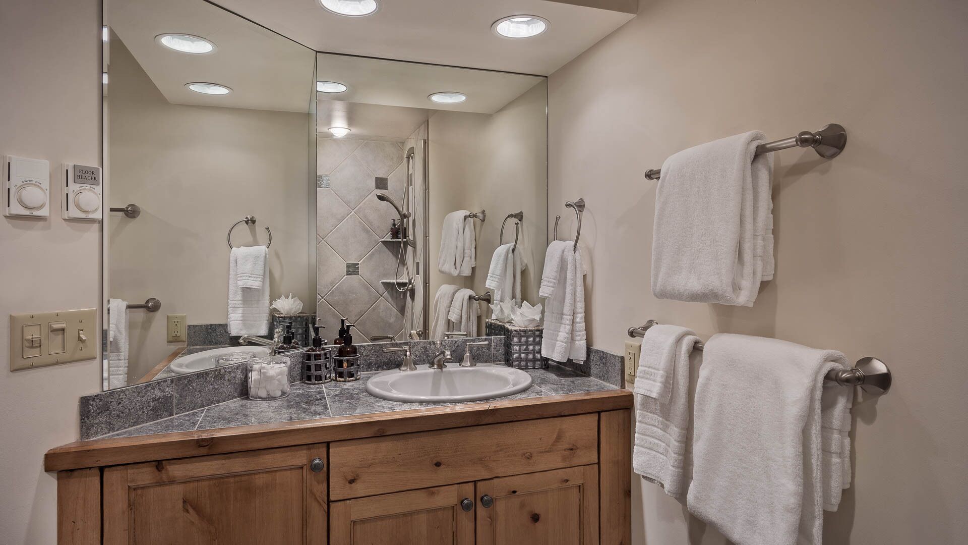 A bathroom with a wooden vanity, a large mirror, a sink, and multiple towels hanging on a rack.