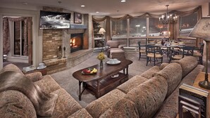 Un salon chaleureux avec une cheminée, des fauteuils confortables, un coin repas et une grande fenêtre donnant sur un paysage enneigé.
