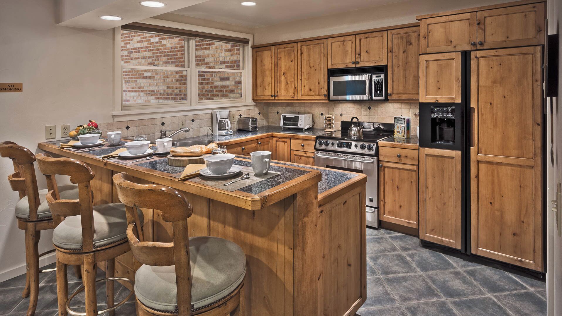 A kitchen with wooden cabinets, a central island with chairs, a microwave, a stove, and a refrigerator.