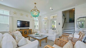 A spacious living room with a large flat-screen TV, a wooden coffee table, white sofas, and wicker chairs. - Driftwood - Vacation Home Near the Beach with a Large Outdoor Area (Santa Rosa Beach)