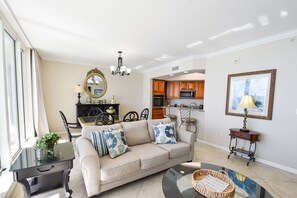 A living room with a sofa, coffee table, and a dining area with chairs and a table. - Updated appliances in beachfront condo w/private balcony! (Destin)