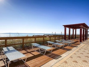 Una terraza de madera con sillones de descanso y una pérgola con vista al océano.