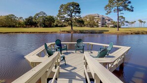 A wooden dock with chairs extending over a calm body of water, surrounded by trees and a golf course in the background. - Beautiful villa with lake views and a floating dock!  271F (Miramar Beach)